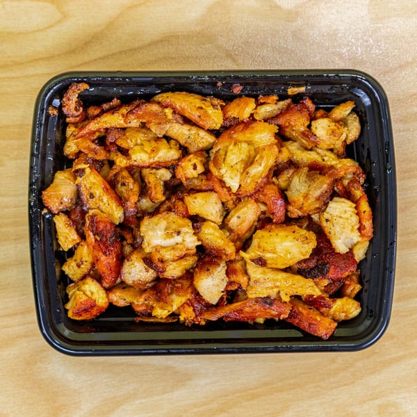 Close-up of a black container filled with golden-brown, seasoned halal chicken pieces on a wooden surface.