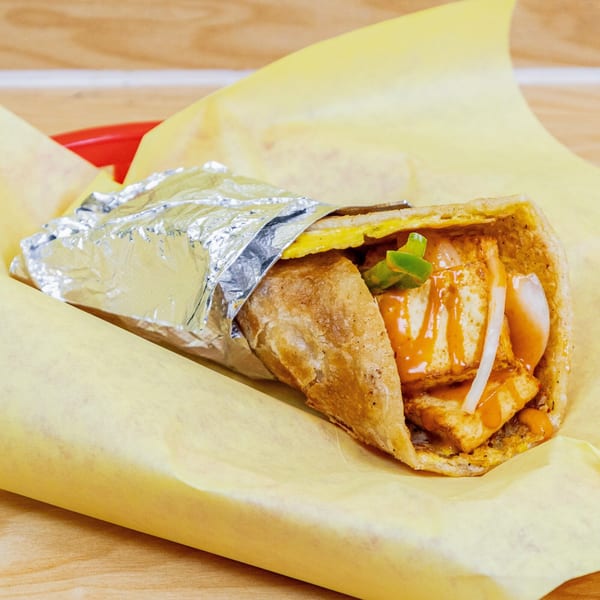 Halal chicken tikka roll with sauce, onions, and peppers, partially wrapped in foil and yellow paper.