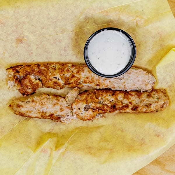 Halal chicken tenders with a side of white dipping sauce on yellow parchment paper.