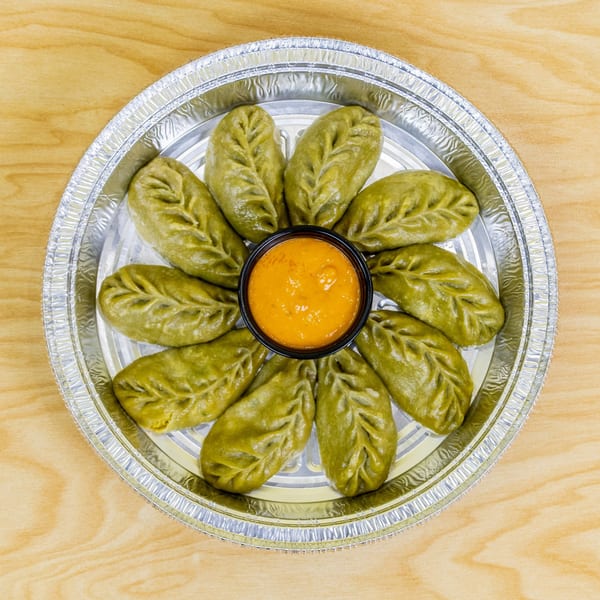 Green dumplings arranged in a circle with a small bowl of orange sauce in the center.