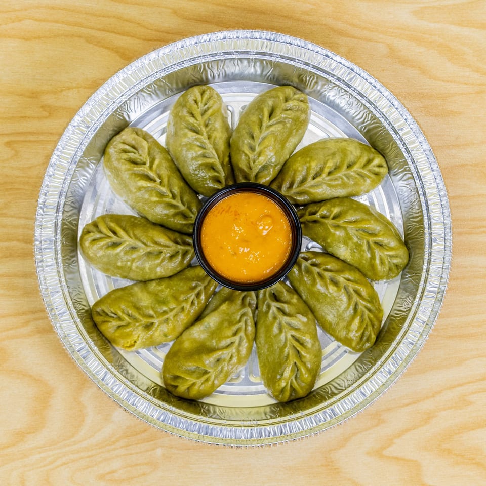 Green dumplings arranged in a circle with a small bowl of orange sauce in the center.