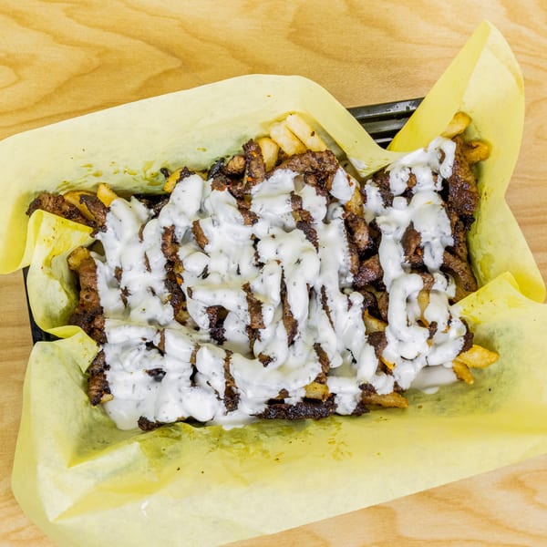 Halal snack pack with seasoned fries, grilled meat, and white sauce in a yellow paper-lined tray.