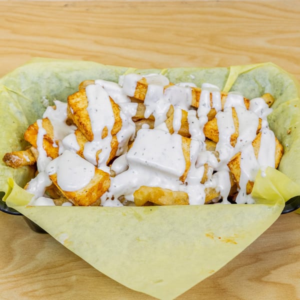 Halal chicken and fries drizzled with white sauce, served in a yellow paper-lined basket.