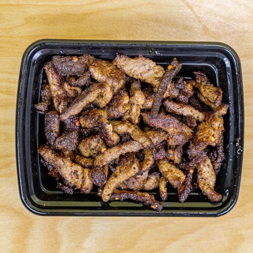 Close-up of a black takeout container filled with crispy, seasoned halal beef strips.