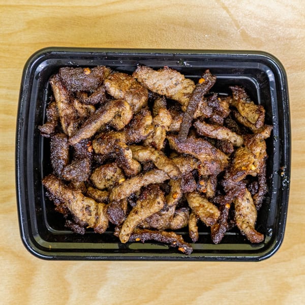 A black takeout container filled with crispy, browned halal beef strips on a light wooden surface.