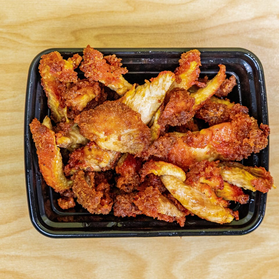 Close-up of crispy, golden-brown halal fried chicken pieces in a black takeout container.